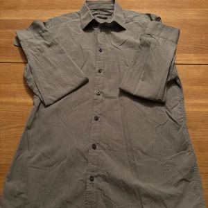 Grå slim fit skjorta Tiger of Sweden - Snygg grå skjorta från Tiger of Sweden i slim fit-modell. Skjortan har klassisk krage, långa ärmar och knäppning framtill. Perfekt för dig som gillar stilrena och enkla plagg med en modern passform.