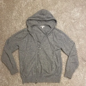 Grå hoodie med dragkedja från BARLUCIO - Mysig grå hoodie från BARLUCIO med hel dragkedja, huva och snörning. Tröjan har långa ärmar, ribbade muddar och två fickor framtill. Perfekt för chill dagar eller när du vill ha en enkel och stilren look. Väldigt bra skick, finns inga defekter!