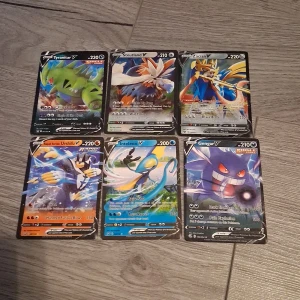 Pokémon V-kort samling (6 st) - Samling med 6 coola Pokémon V-kort: Tyranitar, Stoutland, Zacian, Urshifu, Inteleon och Gengar. Perfekt för dig som vill boosta din samling eller spela med kraftfulla och snygga kort. Färgstarka motiv och höga HP gör dessa till favoriter bland unga Pokémon-fans!