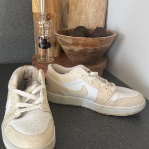 Nike sneakers i beige och vitt - Snygga Nike sneakers i en fräsch kombination av beige och vitt. Skorna har klassisk låg profil, rund tå och snörning. Perfekta för dig som gillar stilrena och neutrala färger. Tillverkade i skinn och syntet för en clean look.
