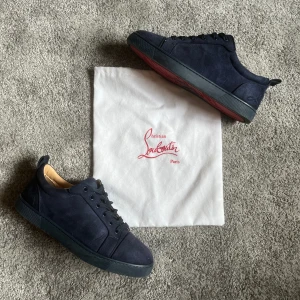 Christian Louboutin - Snygga mörkblå sneakers från Christian Louboutin i mocka med klassisk röd sula och svarta snören. Skorna har en stilren design med rund tå och platt sula. Perfekta för dig som vill ha något exklusivt och unikt i garderoben.