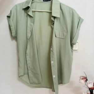 Ljusgrön skjorta - Snygg ljusgrön skjorta från Shein med korta ärmar och klassisk krage. Skjortan har knappar framtill och en bröstficka som detalj. Perfekt för en avslappnad och trendig look.