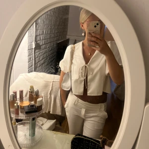 Vit croppad blus med knyt - Säljer en vit croppad blus med korta puffärmar och v-ringning. Toppen har en snygg knytning framtill och är tillverkad i ett lätt bomullstyg. Perfekt för dig som gillar en clean och fräsch look.💗💗Är helt oanvänd!