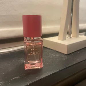 CAIA JOLIE Eau de Parfum 30ml - Snygg parfymflaska från CAIA i modellen JOLIE. Flaskan är rektangulär i glas med en rosa ton och har ett stilrent rosa lock. Texten är i guld och flaskan rymmer 30 ml Eau de Parfum. Perfekt för dig som gillar trendiga dofter och snygg design.
