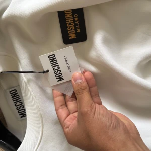 Vit sweatshirt från Moschino Couture - Snygg vit sweatshirt från Moschino Couture med klassisk rund hals och diskret logga i nacken. Tröjan är i mjuk bomull och har en clean look som passar perfekt till jeans eller dressade byxor. Långärmad och riktigt skön att bära.