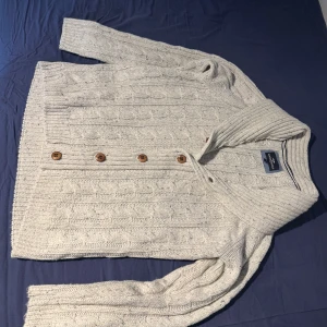 Vit stickad kofta - Säljer en vit/grå stickad kofta med lite små svarta prickar från Hampton Republic i storlek M. Koftan har snygga mönster, träknappar framtill och bred krage.