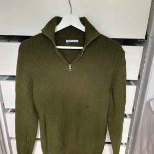 Olivgrön stickad tröja från Zara - Snygg olivgrön stickad tröja från Zara med half zip-dragkedja i halsen. Tröjan har långärmad passform och är ribbstickad för en cool och avslappnad look. Perfekt för lager-på-lager under hösten och vintern. Fick den för nåt år sen men har använt den 2-3 gånger då den varit för stor och när den väl passade gillade jag inte den.