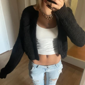 Svart cropped stickad kofta - Svart, croppad kofta med lång ärm och chunky stickad känsla. Koftan har en loose passform och är perfekt att slänga över ett linne eller t-shirt. Tjockt, mysigt material som ger en cool och avslappnad vibe.