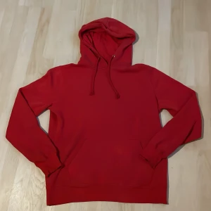 Röd hoodie med huva och ficka - En klassisk röd hoodie med huva och dragsko, samt en stor magficka framtill. Tröjan har långa ärmar och ribbade muddar vid ärmslut och nederkant. Perfekt för en chill och avslappnad stil.