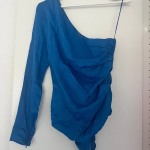 Blå oneshoulder body från Zara - Snygg blå body från Zara med oneshoulder-design och lång ärm. Har draperade detaljer längs sidan.