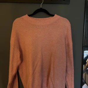 Ljusrosa stickad tröja med rund hals - Mysig ljusrosa stickad tröja med rundad hals och långa ärmar. Tröjan har en enkel och clean design utan mönster eller detaljer, perfekt för dig som gillar en chill och soft stil. Materialet är mjukt och känns skönt mot huden.