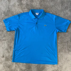 Lacoste piké - Snygg blå pikétröja från Lacoste med klassisk krage och knappslå. Perfekt för en avslappnad stil. Den har korta ärmar och det ikoniska krokodilemblem på bröstet. Pikén kostar cirka 1100 kr nypris och den är perfekt för finare tillfällen eller på golfbanan! Modellen är 183 cm!😉Tröjan är i storlek M-L