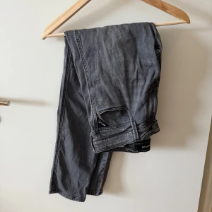 Replay grå jeans straight fit - Snygga grå jeans från Replay med klassisk femficksdesign och raka ben. Jeansen har svarta detaljer på bakfickan och en tydlig Replay-patch. Perfekta för dig som gillar en stilren och avslappnad look.