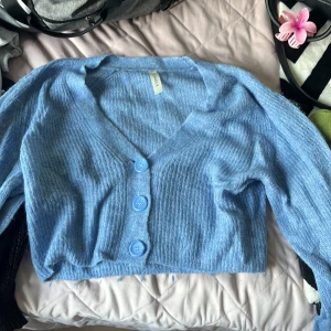 Ljusblå ribbad kofta från Monki - Superfin ljusblå kofta från Lindex med ribbad struktur och tre stora knappar framtill. Koftan är croppad och har v-ringad hals samt långa ärmar. Perfekt att slänga över en topp för en chill look.