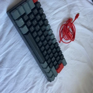 Tangentbord  bra skick  - Bilderna visar ett mekaniskt tangentbord av modellen NOS C450 med en röd USB-kabel. Tangentbordet har en kompakt layout och stilrena grå och röda tangenter. Perfekt för gaming eller studier vid datorn. Snygg design som passar unga och teknikintresserade. Jättebra skick👍👌🔥