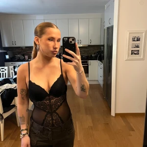 Svart spetsig body med mesh från HM - Säljer en svart body  med tunna axelband, spetsdetaljer framtill och meshpartier på sidorna och ryggen. Toppen är tight och har en djup urringning samt öppen rygg. Bodyn är från hm och är i storlek S