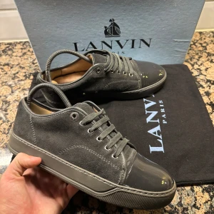 Grå sneakers från Lanvin i mocka och lack - Säljer ett par grå sneakers från Lanvin med ovandel i mocka och lackad tå. Snygg och stilren design med exklusiv känsla. Limited edition. Passar dig med storlek 40-41, är storlek uk5 (Lanvin är stora i storleken). Fråga gärna-svarar snabbt! Orginal pris 5000kr+.