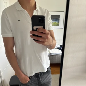 Vit pikétröja från J.Lindeberg - Klassisk vit pikétröja från J.Lindeberg med liten svart logga på bröstet. Tröjan har krage, korta ärmar och knäppning framtill. Tillverkad i bomull för en skön och luftig känsla. Perfekt till jeans eller shorts för en clean look.