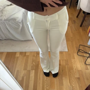 Vita lågmidjade kostymbyxor (Långa) - Snygga vita kostymbyxor med bootcut modell och låg midja. Byxorna har fickor fram och bak. Perfekta för en clean och stilren look. Ganska tunnt material. Långa byxor med en innerbenslängd på ca 90cm🤍 Liten i storleken så de passar en som har storlek XS🤍