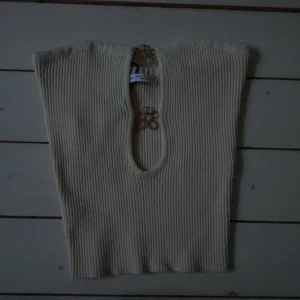 Beige ribbad tubtopp från Bershka - Superfin beige ribbad tubtopp från Bershka i storlek XS. Toppen har en snygg cut-out framtill med dekorativa guldfärgade blommor som detalj. Perfekt att styla med jeans eller kjol för en trendig look. Aldrig använd