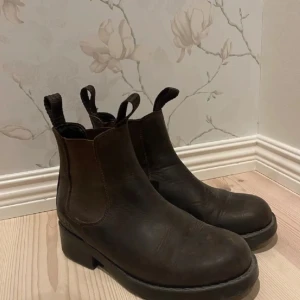 Bruna Johnny Bulls boots i skinn - Snygga bruna Johnny Bulls boots i skinn med rund tå och kraftig platt sula. Resår på sidorna och dragflikar både fram och bak gör dem enkla att ta på. Perfekta för dig som gillar en klassisk och stilren look.
