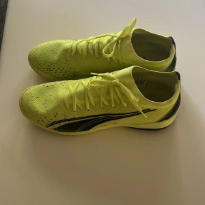 Gula fotbollsskor från Puma - Snygga fotbollsskor från Puma i en riktigt poppig gul färg med svarta detaljer och logga på sidan. Ovandelen är i mesh-liknande syntetmaterial för bra andningsförmåga och passform. Skorna har snörning och en platt sula som ger bra grepp på planen.