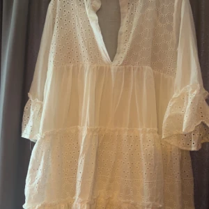 Vit volangklänning med spetsdetaljer - Superfin vit kortklänning med volanger och broderade spetsdetaljer. Djup v-ringning och vida ärmar med volangkant ger en romantisk vibe. Perfekt för sommarens alla tillfällen!