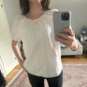 Vit broderad blus med knyt i ryggen - Supersöt vit blus med broderade blommor och korta puffärmar🥰 Blusen har rund halsringning och knytning i ryggen som är öppen🤩 Den har fått en lite gulare färg vid halsen😶‍🌫️