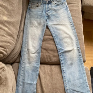 Levi's 501 ljusblå jeans 28/32 - Klassiska Levi's 501 jeans i ljusblå tvätt med raka ben och normal passform. Jeansen har fem fickor, knappgylf och den ikoniska röda Levi's-taggen vid bakfickan. Perfekta för en avslappnad och tidlös stil. Köpte jeansen för 1200 kr och de är i ett väldigt fint skick.