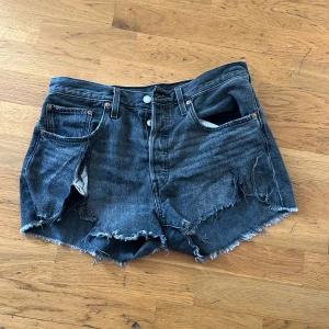 Levi's 501 svarta jeansshorts - Svarta jeansshorts från Levi's modell 501 med råa, fransiga kanter och slitna detaljer framtill. 