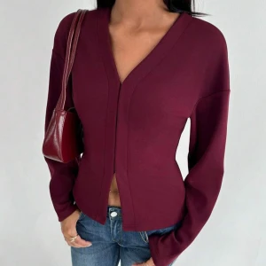 Vinröd v-ringad kofta - Snygg vinröd kofta med v-ringning och lång ärm. Modellen är figurnära och har en stilren design utan synliga knappar. Perfekt att matcha med jeans eller kjol för en trendig look .