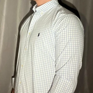Rutig skjorta från Ralph Lauren - Perfekt för varma dagar!☀️🌞Snygg rutig skjorta från Ralph Lauren i ljusblått och vitt. Klassisk button-down krage, långärmad och med broderad logga på bröstet. Skjortan är i bomull och har normal passform. Perfekt för en clean look.
