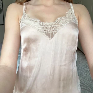 Champagnefärgad linnetopp med spets H&M - Supersöt champagnefärgad/ross linnetopp från H&M med tunna axelband och vacker spetsdetalj fram och bak. Sidenliknande material som känns lyxigt och mjukt mot huden. Perfekt att styla med jeans eller kjol för en trendig look.