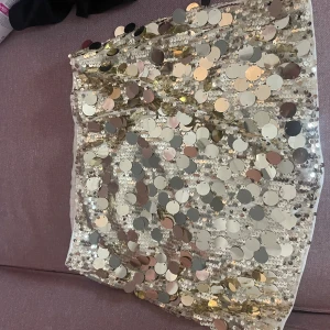 Guldig paljettkjol med stora paljetter - Superglittrig kort kjol täckt av stora guld-  paljetter. Kjolen har en tajt passform och är fodrad och känns riktigt festlig med sitt skimrande material. Säljer eftersom jag köpte i för stor storlek. Aldrig använd
