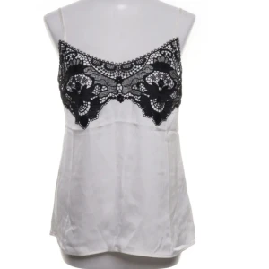 Vit topp med svart spets H&M - Supersnygg vit linnetopp från H&M med tunna axelband och svart spetsdetalj över bysten. Toppen är gjord i mjuk polyester och har en feminin, elegant look som passar perfekt till jeans eller kjol. Köpt i bra skick från sellpy och använd fåtal gånger!