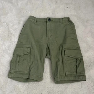 Gröna cargoshorts från Jack & Jones - Snygga gröna cargoshorts från Jack & Jones med flera praktiska fickor på sidorna och bak. Klassisk midja med knapp och dragkedja, samt bälteshällor. Perfekta för chill dagar eller äventyr utomhus. Tillverkade i mjuk bomull för skön känsla.
