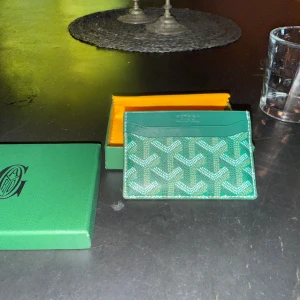 Grön fin plånbok med mönster - Säljer en grön plånbok med ikoniska och  grafiska mönster i vitt och grönt. Plånboken är tunn och smidig, perfekt för kort och sedlar. Kommer med original ask och tygpåse. Riktigt snygg accessoar för dig som gillar exklusiva detaljer. Extremt bra pris för korthållare då köpt på rea!!!!