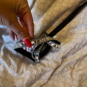 Svart bälte med glittriga stenar - Snyggt svart bälte med glittriga, silvriga stenar längs hela bandet. Bältet har en smal form och detaljer i silver som ger en riktigt festlig och trendig look. Perfekt accessoar för att lyfta din outfit.