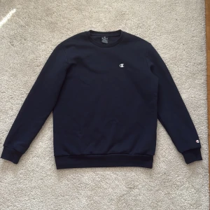 Mörkblå sweatshirt från Champion - Säljer en stilren mörkblå sweatshirt från Champion i storlek small. Tröjan har rund hals, långa ärmar och diskret Champion-logga på bröstet och ärmslutet. Perfekt för en chill och sportig look. Materialet är mjukt och skönt, troligtvis bomull och polyester. 