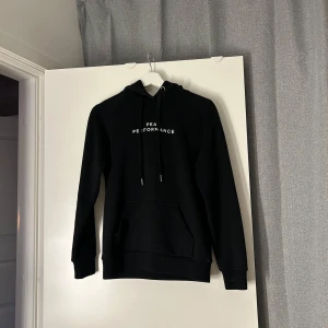 Svart hoodie från Peak Performance - Svart hoodie från Peak Performance med vit logga på bröstet. Klassisk känguruficka, dragsko i huvan och mjukt, fleeceliknande foder. Perfekt för chill dagar eller när du vill ha en clean och stilren look.🩷