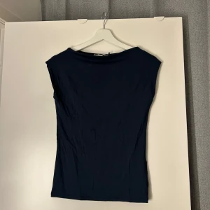 Mörkblå topp från 157, XS - Enkel och stilren mörkblå topp från 157 i storlek XS. Toppen har en rak, något loose passform och är ärmlös med bredare axelparti. Perfekt att matcha med jeans eller kjol för en clean look.❤️