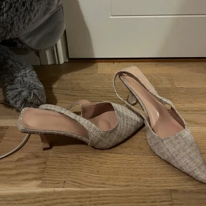 Beige pumps med spetsig tå och klack - Snygga pumps i beige med spetsig tå och låg klack. Skorna har en textilstruktur med diskret glittriga inslag och öppen häl med rem. Perfekta för dig som gillar stilrena och trendiga detaljer. Dem är aldrig använda!!