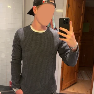 Mörkgrå stickad tröja herr - Säljer en mörkgrå stickad tröja med rund halsringning och lång ärm. Tröjan har en diskret struktur i materialet och passar perfekt till jeans eller chinos. Enkel och stilren design som funkar till många olika outfits.
