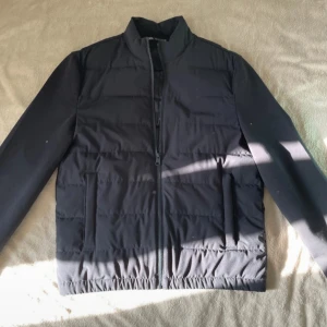 Zara jacka - Snygg svart pufferjacka med raka linjer och hög krage. Jackan har hel dragkedja framtill och två sidofickor. Perfekt för dig som gillar en stilren look och vill hålla värmen under kyliga dagar.