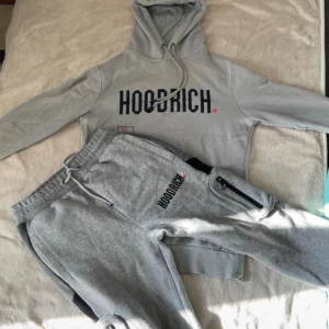  Hoodrich tracksuit - Snygg grå tracksuit från Hoodrich med stor svart logga framtill. Tröjan har huva med dragsko och långa ärmar. Perfekt för en chill och avslappnad stil. Mjuk och skön känsla tack vare bomullsmaterialet.