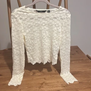 Vit spetsblus - Superfin vit spetsblus från Vero Moda med långärmad design och blommigt spetsmönster. Blusen har vågiga kanter vid ärmslut och nederkant, vilket ger en extra söt touch. Perfekt att styla med jeans eller kjol för en trendig look.