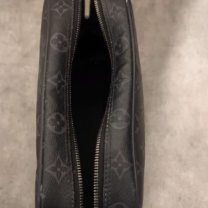 Louis Vuitton svart monogram axelväska - Snygg svart axelväska från Louis Vuitton äkta med klassiskt monogrammönster i grått. Väskan har rektangulär form, dragkedja upptill och är tillverkad i skinn. Perfekt för dig som vill ha en stilren och ikonisk accessoar.