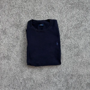 Ralph Lauren tröja mörkblå - Klassisk mörkblå tröja från Ralph Lauren med rund halsringning och diskret broderad logga på bröstet. Tröjan är långärmad och tillverkad i mjuk bomull, perfekt för en clean och stilren look. Observa tappad etikett 