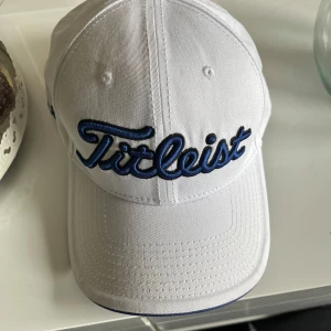 Titleist keps vit/blå - Snygg vit keps från Titleist med broderad blå logga framtill. Klassisk böjd skärm och justerbar rem baktill för perfekt passform. Tillverkad i bomull, perfekt för golf eller en sportig look. Har använt den några fåtal gånger så den är i bra skick! Mvh Nils🙌⛳️Om du köper golfbollar med så kan priset gå ner. 