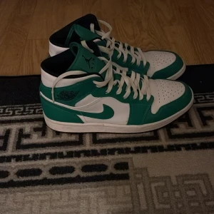 Nike Air Jordan 1 Mid grön/vit EUR 44 - Nike Air Jordan 1 Mid i fräscha gröna och vita färger. Klassisk siluett med snörning, perforerad tå och ikoniska Jordan-loggor på sidan och plösen. Ovandel i skinn och syntet, vit sula och svart innerfoder. Perfekta för dig som vill sticka ut med stil.